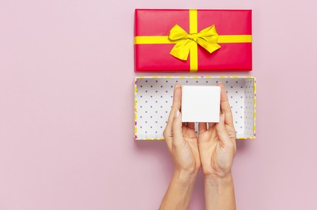 Woman hands holding present red box with gold ribbon on pink background Flat lay top view. Present for birthday, surprise, valentine day, Christmas New Year. Congratulations background copy space.の写真素材