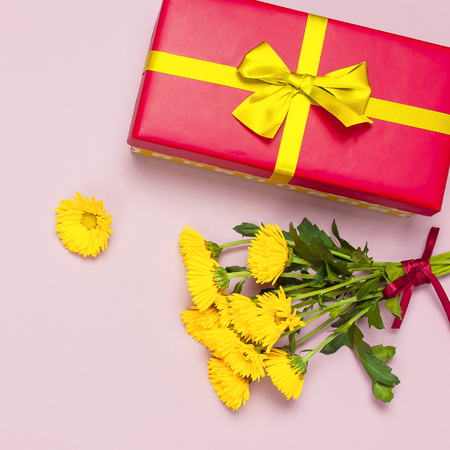 Red gift box with gold ribbon and yellow chrysanthemums on pink background top view flat lay. Holiday concept, birthday gift valentine day or anniversary. Congratulations background copy space.の写真素材