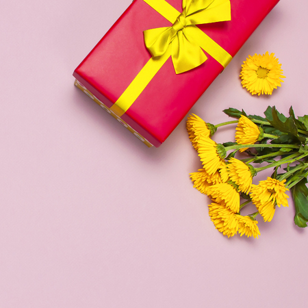 Red gift box with gold ribbon and yellow chrysanthemums on pink background top view flat lay. Holiday concept, birthday gift valentine day or anniversary. Congratulations background copy space.の写真素材
