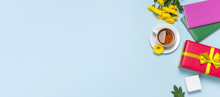 Red gift box with gold ribbon yellow chrysanthemums cup of tea notebook on blue background top view flat lay. Holiday concept, birthday gift, valentine day or anniversary Congratulations backgroundの写真素材