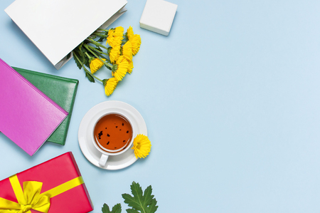 Red gift box with gold ribbon yellow chrysanthemums cup of tea notebook on blue background top view flat lay. Holiday concept, birthday gift, valentine day or anniversary Congratulations backgroundの写真素材