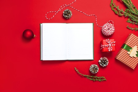 Open notebook with blank pages, gift boxes, fir branches, ball on red background flat lay top view. Christmas planning concept Holiday decorations 2019 Goals. New Year, Christmas winter decorationの写真素材