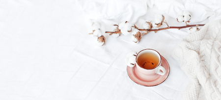Cup of hot tea, branch of delicate cotton and knitted plaid sweater in bed with white linens. Cozy morning breakfast at home Lifestyle gentle female background Copy Space autumn winter conceptの写真素材
