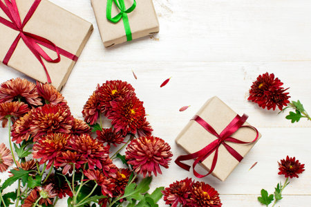 Red autumn chrysanthemum flowers and gift boxes with ribbons on white wooden background. Top view...