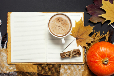 Opened notebook, pumpkin, cup of pumpkin cocoa or coffee, cinnamon, yellow autumn maple leaf, checkered plaid on black background top view copy space. Autumn flat lay background. Autumn, fall halloween concept.の写真素材