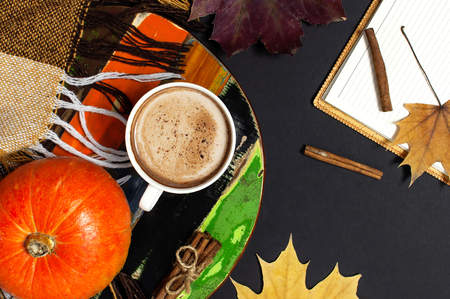 Opened notebook, pumpkin, cup of pumpkin cocoa or coffee, cinnamon, yellow autumn maple leaf, checkered plaid on black background top view copy space. Autumn flat lay background. Autumn, fall halloween concept.の写真素材