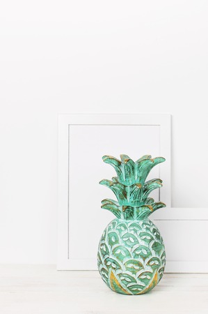 Wooden empty frames for a photo and a wooden emerald pineapple on a background of a white wall. Blank paper frames modern home decor mock-up. Interior background.の写真素材