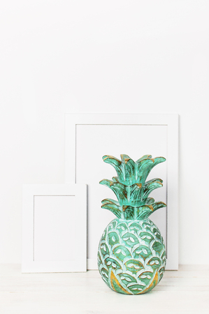 Wooden empty frames for a photo and a wooden emerald pineapple on a background of a white wall. Blank paper frames modern home decor mock-up. Interior background.の写真素材