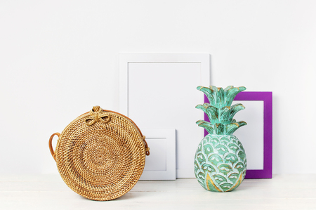 Wooden empty frames for a photo, wooden emerald pineapple, fashionable handmade natural organic rattan bag on a background of a white wall. Blank paper frames, accessories in the house, modern home decor mock-up Interior background.の写真素材