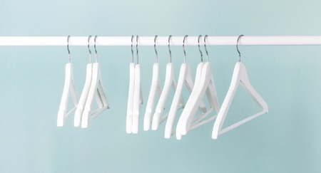 Many wooden white hangers on a rod, isolated on blue turquoise wall background. Store concept, sale, design, empty hanger. Place for text Soft focus.の写真素材