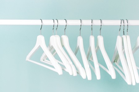 Many wooden white hangers on a rod, isolated on blue turquoise wall background. Store concept, sale, design, empty hanger. Place for text Soft focus.の写真素材