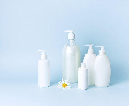 Cosmetic bottle containers with chamomile flowers on a blue minimalistic background flat lay. Blank label for branding mock-up. Natural beauty product conceptの写真素材