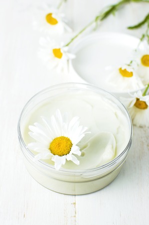 Opened plastic container with cream and chamomile flower on a light background. Herbal dermatology cosmetic hygienic cream Spa concept organic cosmetic Natural beauty productの写真素材