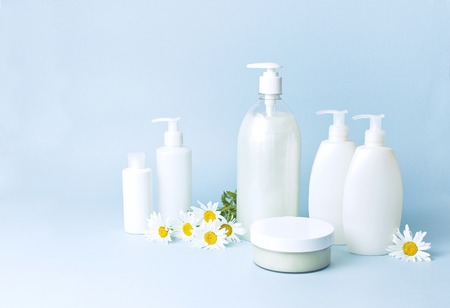 Cosmetic bottle containers with chamomile flowers on a blue minimalistic background flat lay. Blank label for branding mock-up. Natural beauty product conceptの写真素材