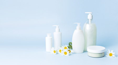 Cosmetic bottle containers with chamomile flowers on a blue minimalistic background flat lay. Blank label for branding mock-up. Natural beauty product conceptの写真素材