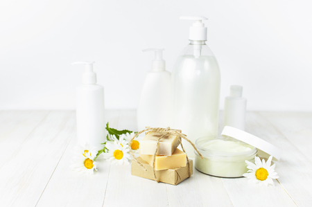 Opened plastic container with cream, handmade soaps, white cosmetic bottle containers and chamomile flower on a white background. Herbal dermatology cosmetic Spa concept organic cosmetic Natural beauty productの写真素材