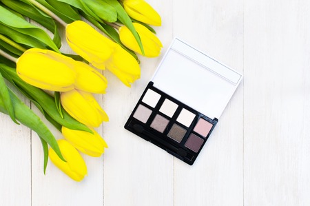 Decorative cosmetics for make-up set of makeup shadows and yellow tulips on a light wooden background top view Flat lay. Makeup Accessories with copy spaceの写真素材