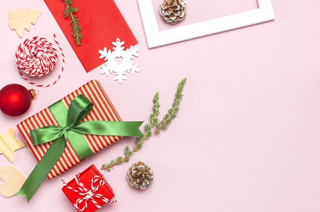 Christmas composition. White photo frame, red envelope, fir branches, cones, ball, twine, gift, wooden toys on pink background Flat lay top view. Christmas winter decoration New Year, holiday objectsの写真素材