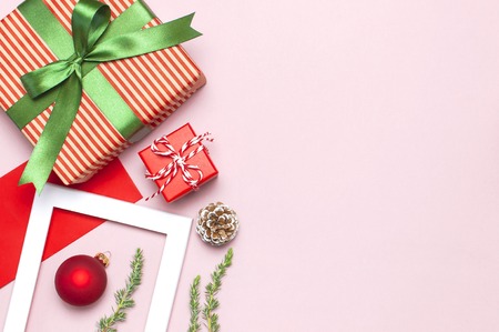 Christmas composition. White photo frame, red envelope, fir branches, cones, ball, twine, gift, wooden toys on pink background Flat lay top view. Christmas winter decoration New Year, holiday objectsの写真素材
