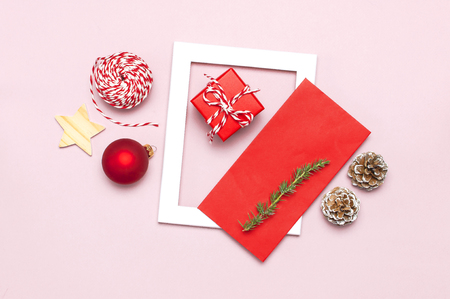 Christmas composition. White photo frame, red envelope, fir branches, cones, ball, twine, gift, wooden toys on pink background Flat lay top view. Christmas winter decoration New Year, holiday objectsの写真素材