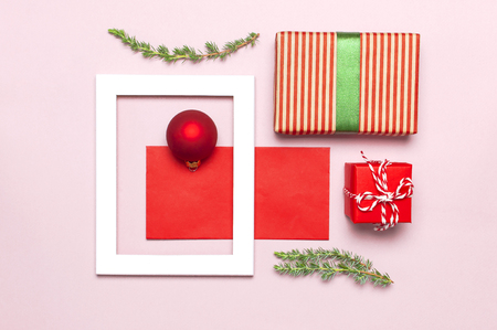 Christmas composition. White photo frame, red envelope, fir branches, cones, ball, twine, gift, wooden toys on pink background Flat lay top view. Christmas winter decoration New Year, holiday objectsの写真素材