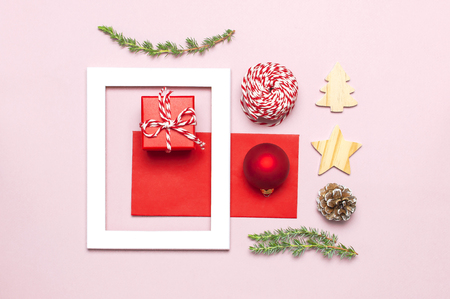Christmas composition. White photo frame, red envelope, fir branches, cones, ball, twine, gift, wooden toys on pink background Flat lay top view. Christmas winter decoration New Year, holiday objectsの写真素材