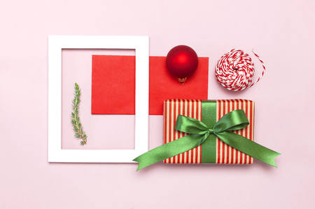 Christmas composition. White photo frame, red envelope, fir branches, cones, ball, twine, gift, wooden toys on pink background Flat lay top view. Christmas winter decoration New Year, holiday objectsの写真素材