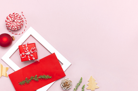 Christmas composition. White photo frame, red envelope, fir branches, cones, ball, twine, gift, wooden toys on pink background Flat lay top view. Christmas winter decoration New Year, holiday objectsの写真素材
