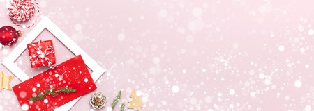 Snowy Christmas composition. White photo frame, red envelope, fir branches, cones ball twine gift wooden toys on pink background Flat lay top view Christmas winter decoration New Year holiday objectsの写真素材
