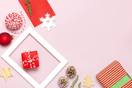Christmas composition. White photo frame, red envelope, fir branches, cones, ball, twine, gift, wooden toys on pink background Flat lay top view. Christmas winter decoration New Year, holiday objectsの写真素材