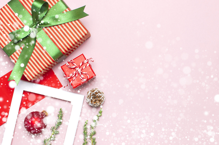 Snowy Christmas composition. White photo frame, red envelope, fir branches, cones ball twine gift wooden toys on pink background Flat lay top view Christmas winter decoration New Year holiday objectsの写真素材