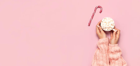 Christmas New Year drink, white mug with marshmallows in female hands in knitted sweater and Candy Cane on pink background top view Flat Lay Winter traditional food. Festive decor celebration Xmasの写真素材