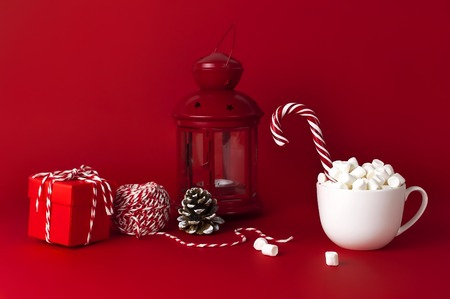 White mug with marshmallows Candy Cane gifts boxes packaging lace flashlight on red background Flat Lay copy space. Winter traditional drink food Festive decor celebration Christmas New Year holidayの写真素材