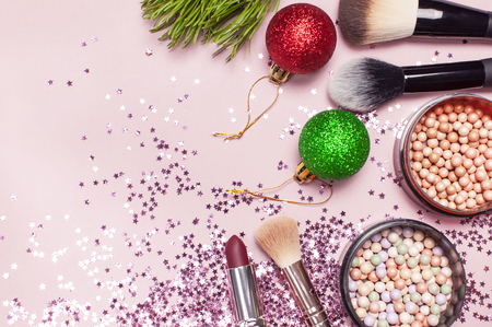 Cosmetic makeup brushes, blush powder, christmas balls, lipstick, holographic glitter confetti in the form of stars on pink background Flat lay top view copy space. Makeup accessories holidayの写真素材