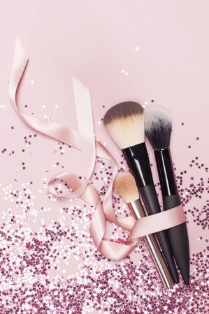 Different Cosmetic makeup brushes with pink ribbon and holographic glitter confetti in the form of stars on pink background Flat lay top view copy space Makeup accessories holiday birthday new year.の写真素材
