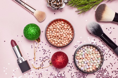 Cosmetic makeup brushes, blush powder, christmas balls, lipstick, holographic glitter confetti in the form of stars on pink background Flat lay top view copy space. Makeup accessories holidayの写真素材