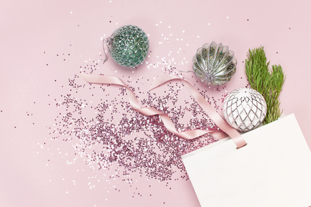 Flat lay top view White gift bag holographic glitter confetti Vintage Christmas New Year balls green pine branches on pink background Greeting card Festive holiday decoration Congratulations xmas.の写真素材