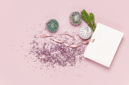 Flat lay top view White gift bag holographic glitter confetti Vintage Christmas New Year balls green pine branches on pink background Greeting card Festive holiday decoration Congratulations xmas.の写真素材