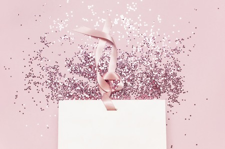 Flat lay top view White gift bag and holographic glitter confetti in the form of stars on pink background. Greeting card Festive holiday pastel backdrop Birthday congratulations Christmas New Yearの写真素材