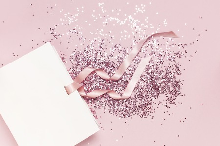 Flat lay top view White gift bag and holographic glitter confetti in the form of stars on pink background. Greeting card Festive holiday pastel backdrop Birthday congratulations Christmas New Yearの写真素材