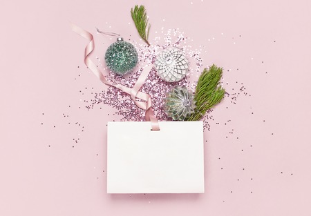 Flat lay top view White gift bag holographic glitter confetti Vintage Christmas New Year balls green pine branches on pink background Greeting card Festive holiday decoration Congratulations xmas.の写真素材