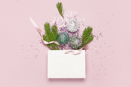 Flat lay top view of White gift bag holographic glitter confetti and green pine branches on pink backgroundの写真素材