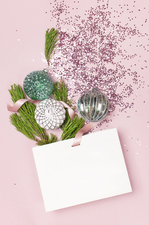 Flat lay top view White gift bag holographic glitter confetti Vintage Christmas New Year balls green pine branches on pink background Greeting card Festive holiday decoration Congratulations xmas.の写真素材