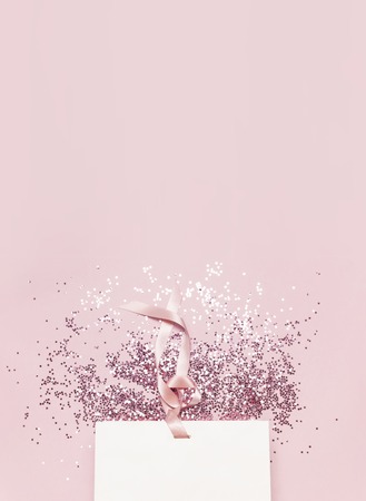 Flat lay top view White gift bag and holographic glitter confetti in the form of stars on pink background. Greeting card Festive holiday pastel backdrop Birthday congratulations Christmas New Yearの写真素材