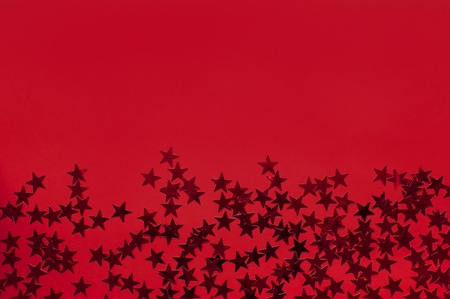 Red holographic glitter confetti in the form of stars on red background Flat lay top view copy space. Festive holiday pastel backdrop. Birthday, congratulations, Christmas New Yearの写真素材