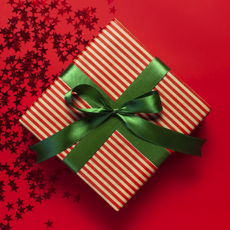 Gift box with green ribbon and holographic glitter confetti form of stars on red background top view flat lay. Holiday concept, birthday gift new year or Christmas gift box presents Xmas holidayの写真素材