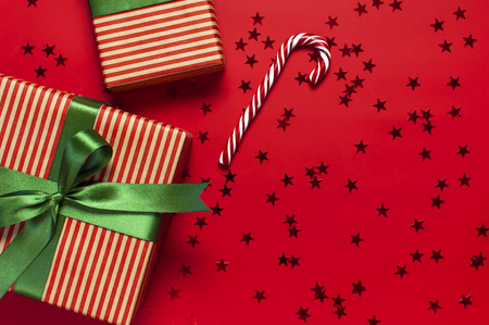 Gift boxes with green ribbon, Candy Cane, glitter confetti form of stars on red background top view flat lay. Holiday concept new year or Christmas gift box, presents Xmas holidayの写真素材