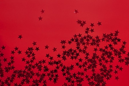 Red holographic glitter confetti in the form of stars on red background Flat lay top view copy space. Festive holiday pastel backdrop. Birthday, congratulations, Christmas New Yearの写真素材