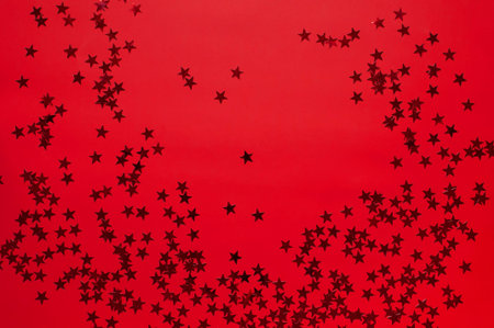 Red holographic glitter confetti in the form of stars on red background Flat lay top view copy...