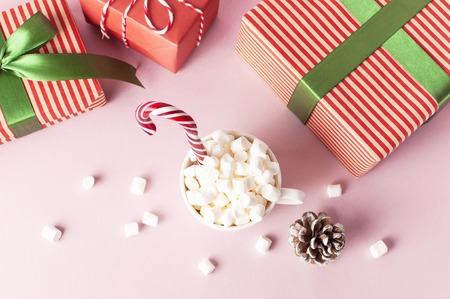 White mug with marshmallows Candy Cane gifts boxes with green ribbon on pink background Flat Lay Winter traditional drink food Festive decor Christmas New Year presents Xmas holiday.の写真素材